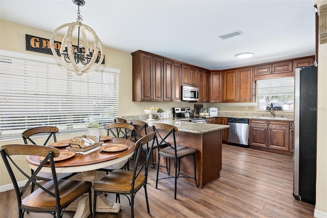 kitchen with stainless steel appliances, dark hardwood / wood-style floors, light stone countertops, sink, and kitchen peninsula