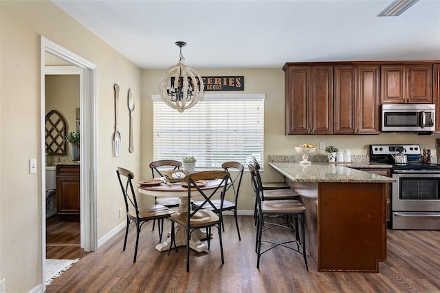 kitchen featuring stainless steel appliances, dark wood-type flooring, decorative light fixtures, and light stone counters