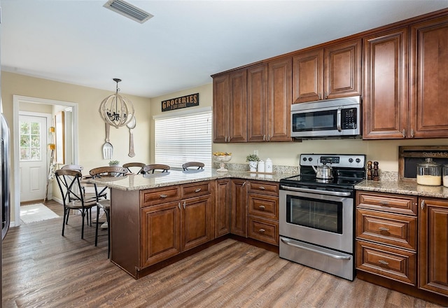 kitchen featuring appliances with stainless steel finishes, dark hardwood / wood-style floors, pendant lighting, light stone countertops, and kitchen peninsula