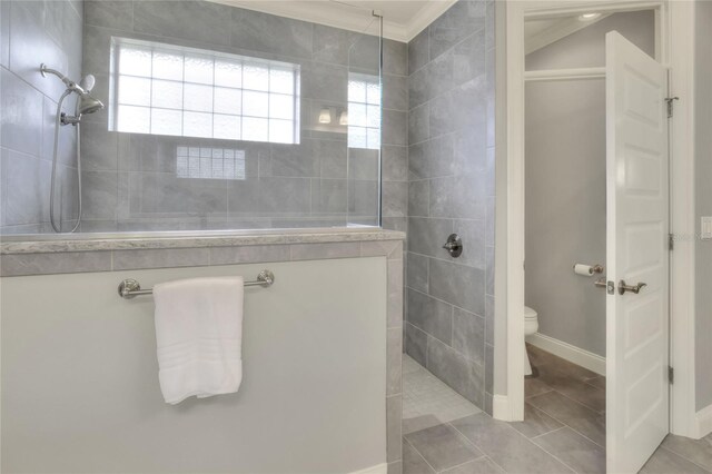 bathroom with toilet, tile patterned flooring, crown molding, and a tile shower