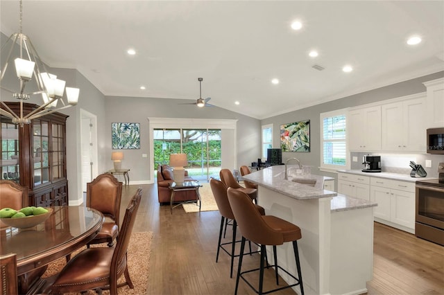 kitchen with pendant lighting, appliances with stainless steel finishes, white cabinetry, an island with sink, and hardwood / wood-style flooring