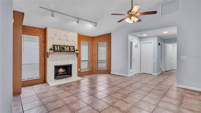 unfurnished living room with lofted ceiling, light tile floors, a stone fireplace, and ceiling fan