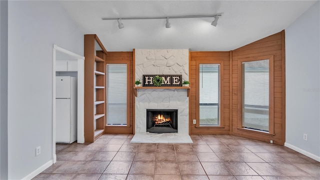 unfurnished living room featuring wooden walls, built in shelves, light tile floors, rail lighting, and a stone fireplace