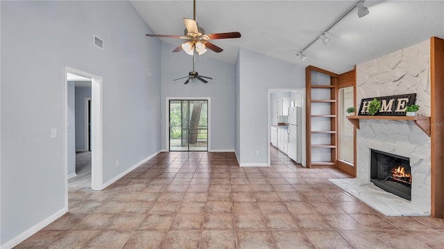 unfurnished living room with a premium fireplace, track lighting, ceiling fan, and light tile floors