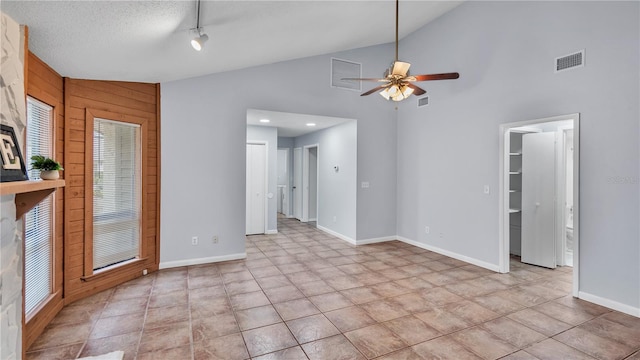 tiled empty room with ceiling fan, plenty of natural light, wood walls, high vaulted ceiling, and a textured ceiling