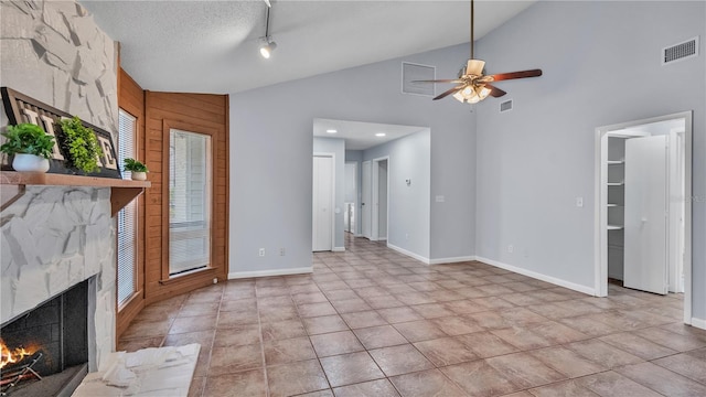 unfurnished living room with ceiling fan, light tile floors, a premium fireplace, a textured ceiling, and wooden walls