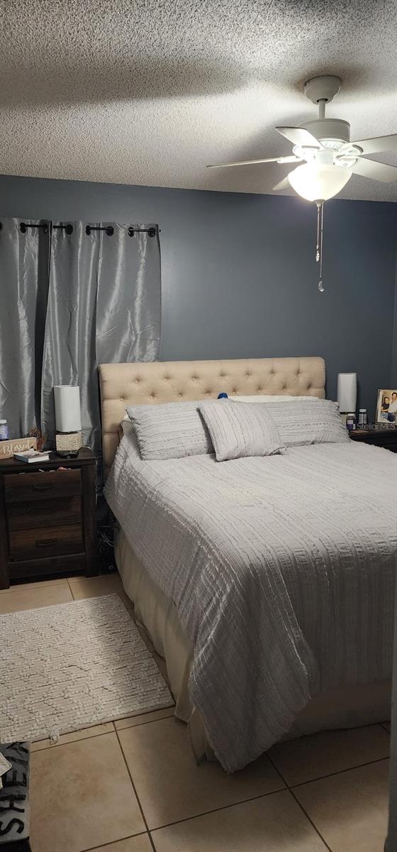 tiled bedroom with ceiling fan and a textured ceiling