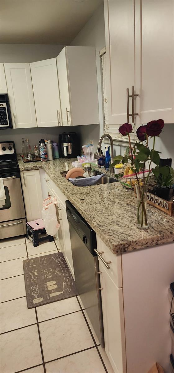 kitchen featuring light tile flooring, stainless steel electric range, white cabinetry, and light stone counters