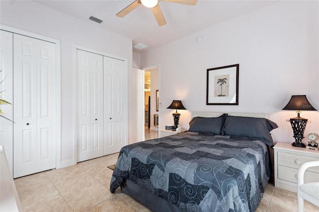 bedroom featuring ceiling fan, multiple closets, and light tile floors