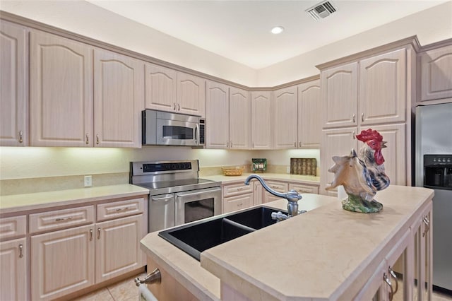 kitchen with light tile flooring, appliances with stainless steel finishes, sink, a center island, and light brown cabinetry