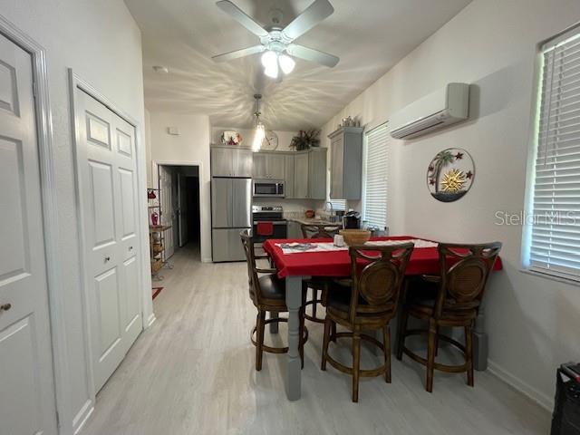 dining room featuring a healthy amount of sunlight, a wall mounted air conditioner, ceiling fan, and light wood-type flooring