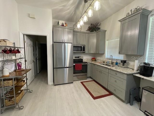 kitchen featuring hanging light fixtures, appliances with stainless steel finishes, sink, light hardwood / wood-style flooring, and gray cabinets