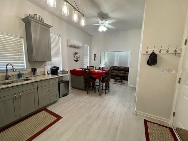 kitchen with ceiling fan, sink, a wall mounted air conditioner, light stone countertops, and light wood-type flooring