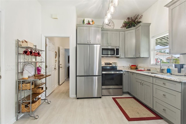 kitchen with sink, gray cabinets, appliances with stainless steel finishes, light stone countertops, and light wood-type flooring