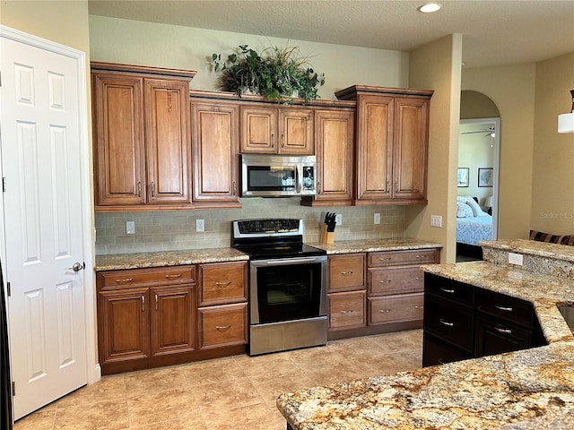 kitchen featuring backsplash, stainless steel appliances, light stone countertops, and light tile floors