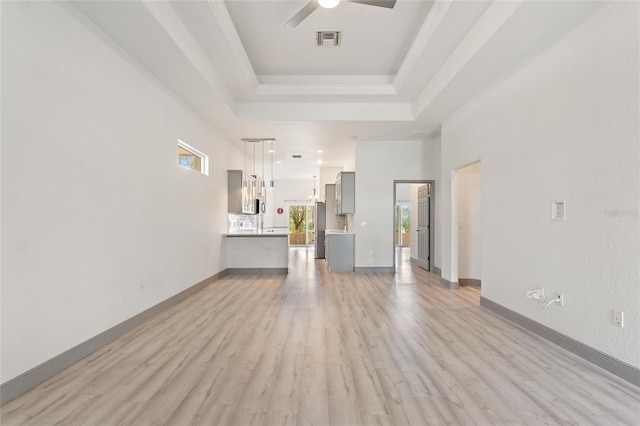 unfurnished living room featuring ceiling fan with notable chandelier, a tray ceiling, and light wood-type flooring