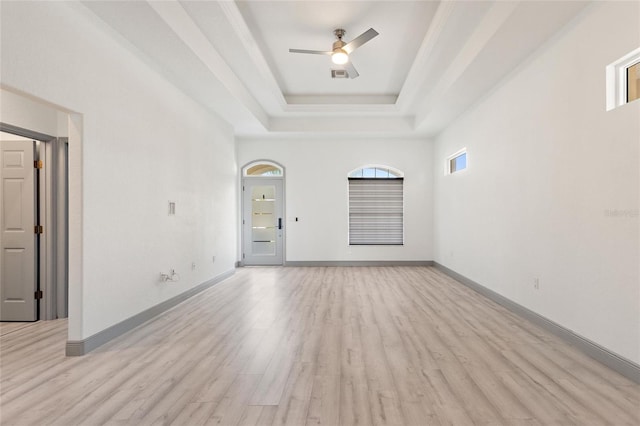 empty room featuring a raised ceiling, ceiling fan, and light wood-type flooring