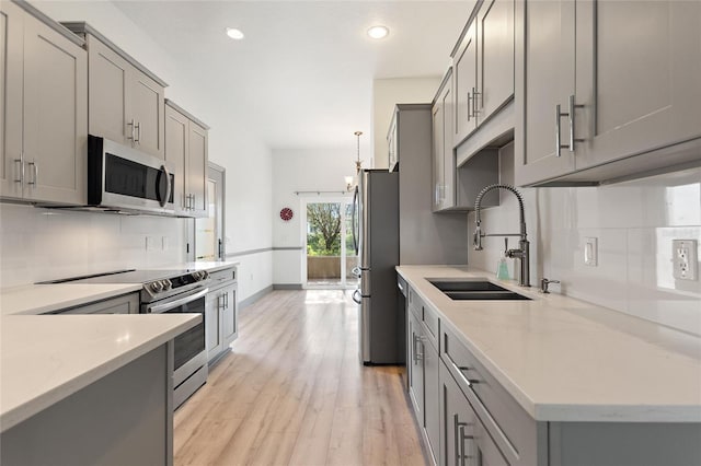 kitchen with gray cabinetry, appliances with stainless steel finishes, sink, light hardwood / wood-style flooring, and tasteful backsplash