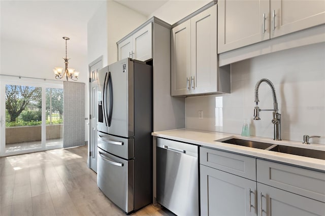 kitchen with a notable chandelier, appliances with stainless steel finishes, light hardwood / wood-style floors, sink, and pendant lighting