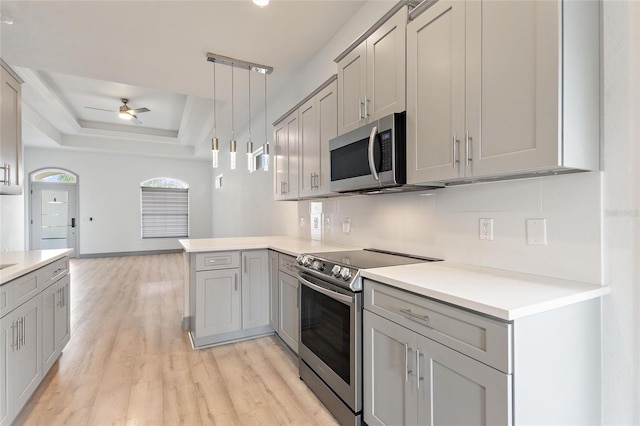 kitchen with ceiling fan, a raised ceiling, appliances with stainless steel finishes, light hardwood / wood-style flooring, and decorative light fixtures