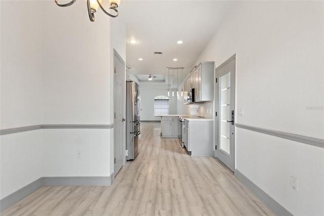 kitchen with gray cabinetry, appliances with stainless steel finishes, an inviting chandelier, decorative light fixtures, and light wood-type flooring