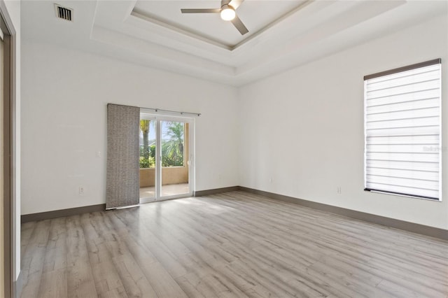 unfurnished room featuring a tray ceiling, ceiling fan, and light hardwood / wood-style flooring