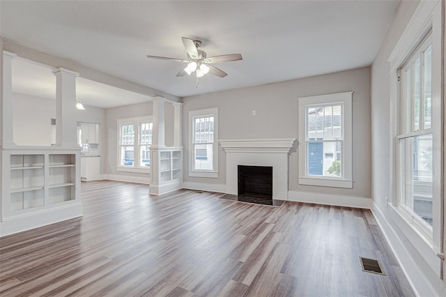 unfurnished living room with a brick fireplace, ceiling fan, decorative columns, and light wood-type flooring