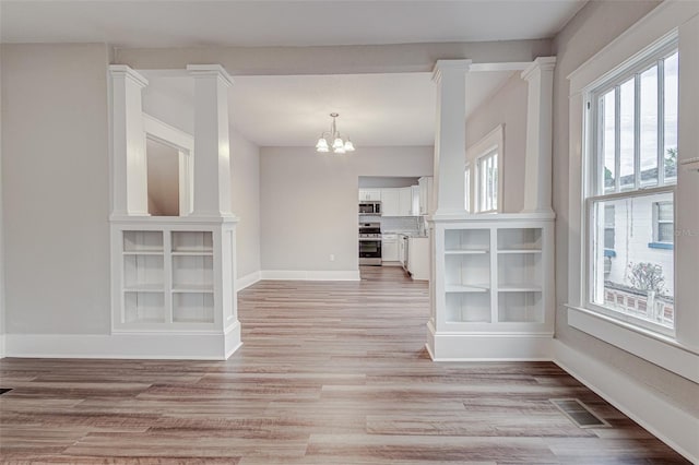 interior space with a chandelier, ornate columns, a wealth of natural light, and light wood-type flooring