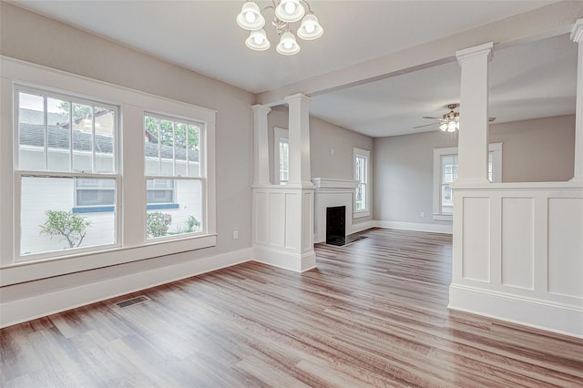 unfurnished living room featuring ornate columns, light hardwood / wood-style floors, and ceiling fan with notable chandelier