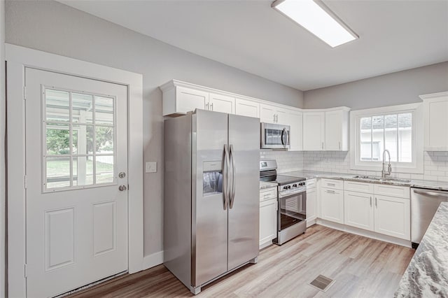 kitchen with white cabinets, appliances with stainless steel finishes, light stone counters, and sink