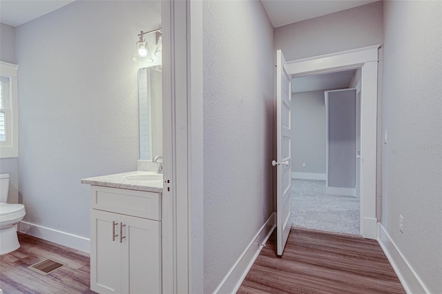 bathroom with toilet, vanity with extensive cabinet space, and hardwood / wood-style flooring