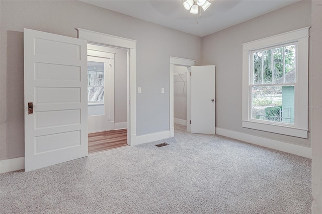 unfurnished bedroom with a closet, a walk in closet, ceiling fan, and light colored carpet