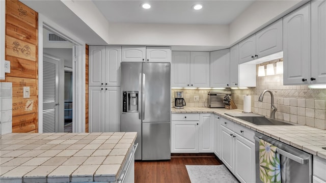 kitchen featuring dark wood-type flooring, appliances with stainless steel finishes, backsplash, tile counters, and sink