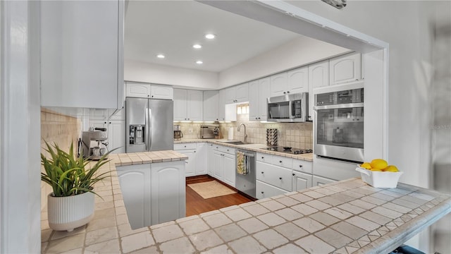 kitchen featuring backsplash, stainless steel appliances, white cabinets, tile counters, and hardwood / wood-style flooring