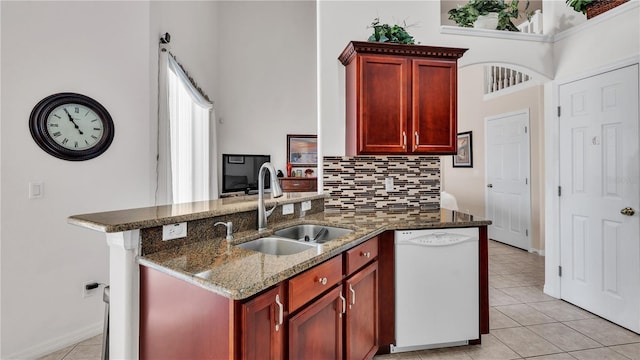 kitchen with sink, light tile floors, dark stone counters, white dishwasher, and tasteful backsplash