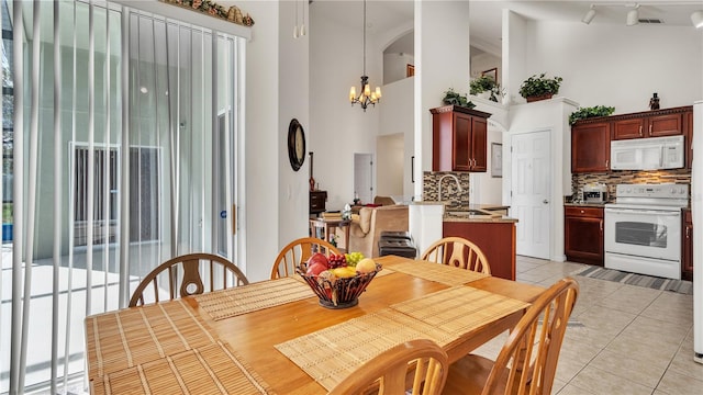 tiled dining room featuring an inviting chandelier, a towering ceiling, rail lighting, and sink