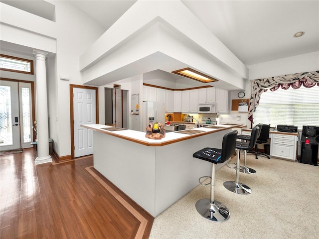 kitchen featuring white cabinets, decorative columns, a breakfast bar area, hardwood / wood-style flooring, and white appliances