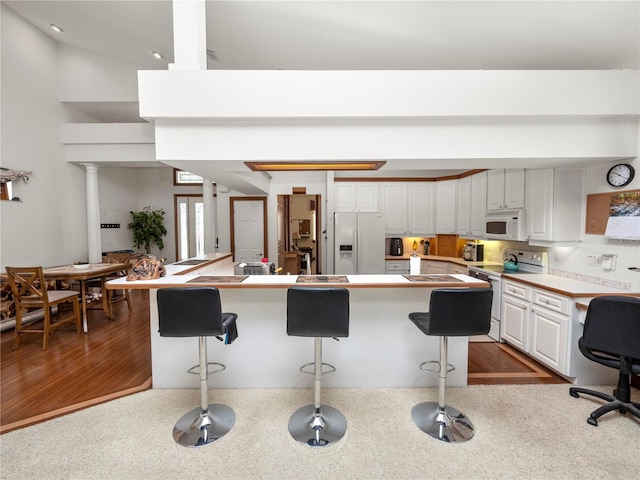 kitchen with a kitchen breakfast bar, white cabinets, dark wood-type flooring, and white appliances