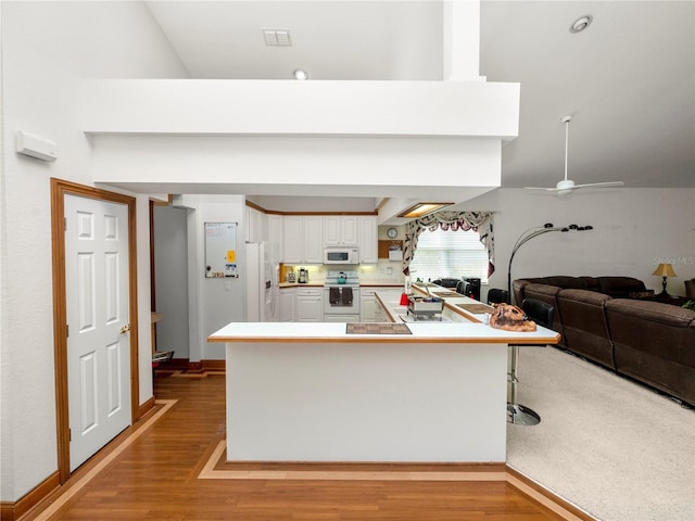 kitchen with white cabinets, white appliances, light carpet, and kitchen peninsula