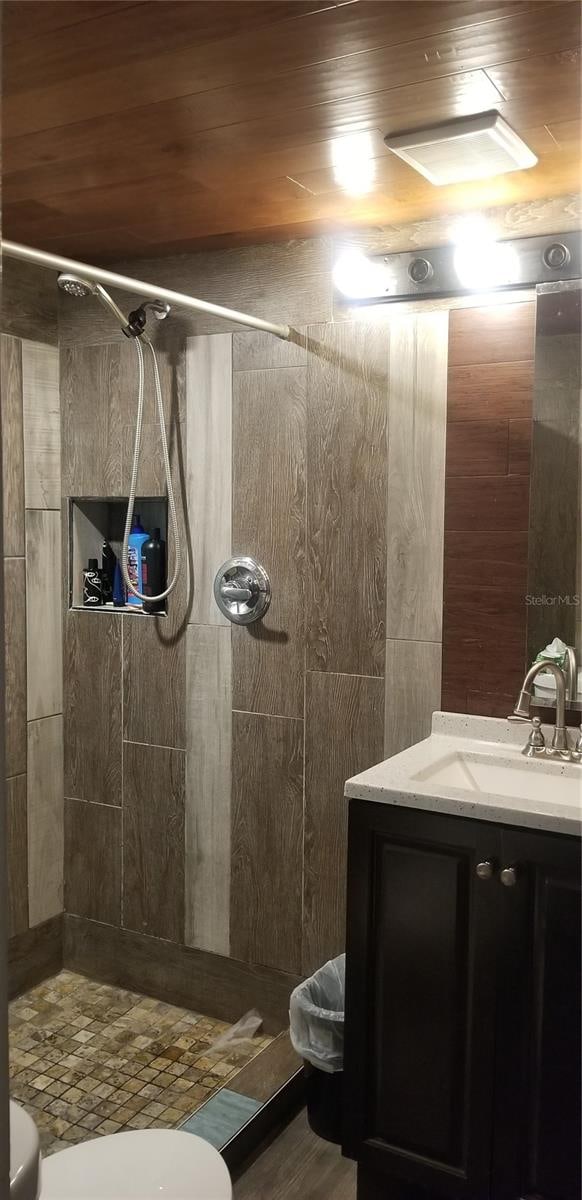 bathroom featuring tiled shower, vanity, toilet, and wood ceiling