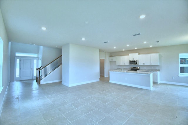 kitchen with light stone counters, stainless steel appliances, sink, white cabinetry, and an island with sink