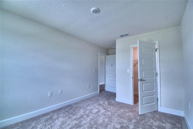 unfurnished bedroom with carpet flooring, a spacious closet, a closet, and a textured ceiling