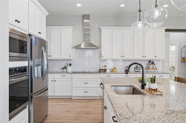 kitchen with wall chimney exhaust hood, white cabinetry, appliances with stainless steel finishes, and sink