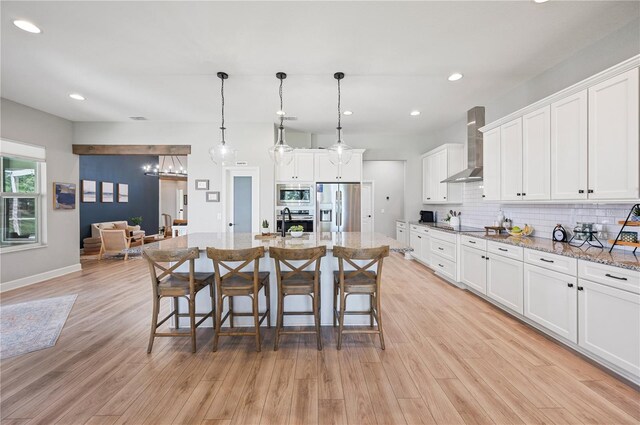 kitchen featuring a center island with sink, wall chimney range hood, stainless steel appliances, and white cabinets