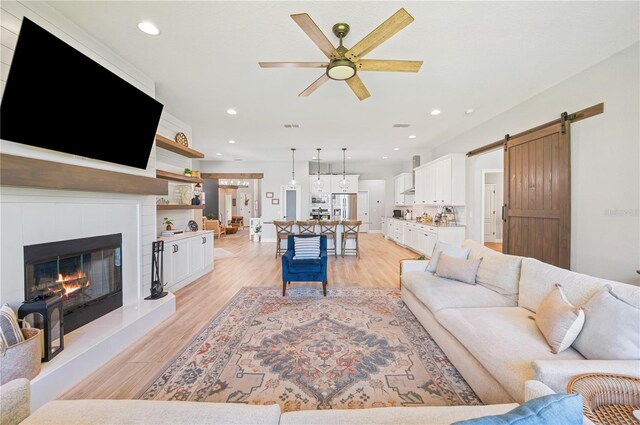 living room with ceiling fan, a fireplace, a barn door, and light hardwood / wood-style floors