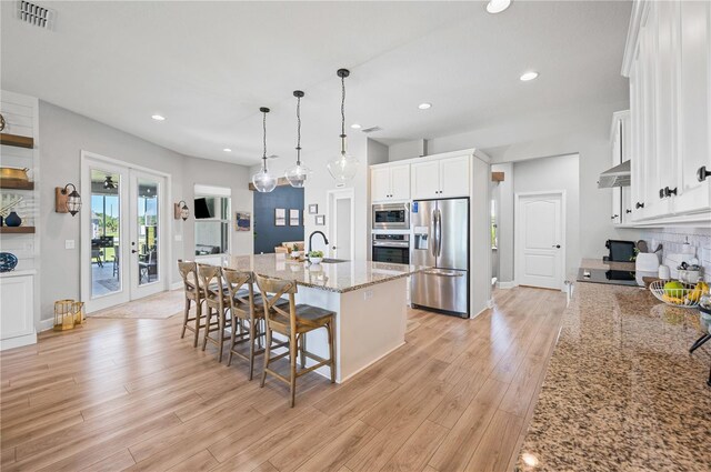 kitchen featuring light hardwood / wood-style floors, white cabinetry, stainless steel appliances, a center island with sink, and light stone countertops