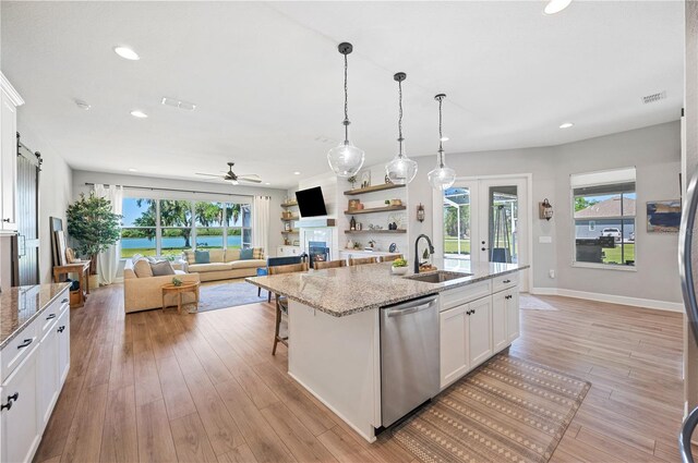 kitchen featuring light stone counters, white cabinets, dishwasher, a center island with sink, and sink