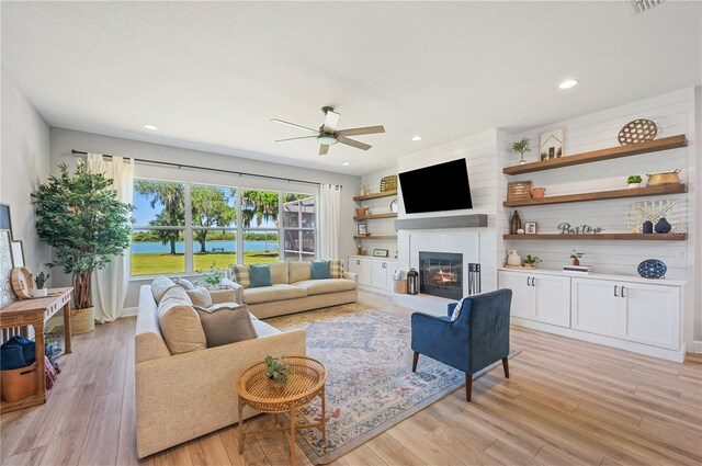 living room featuring a large fireplace, light hardwood / wood-style floors, and ceiling fan