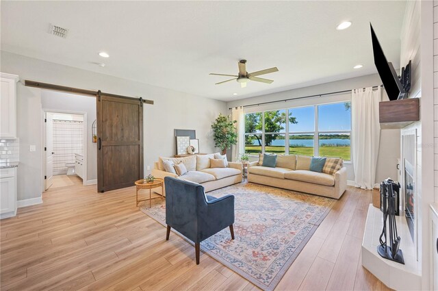 living room with light wood-type flooring, ceiling fan, and a barn door