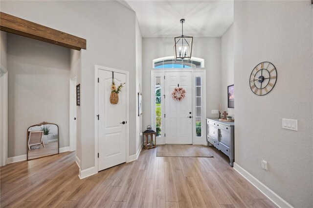 entryway featuring light hardwood / wood-style flooring, a towering ceiling, and an inviting chandelier